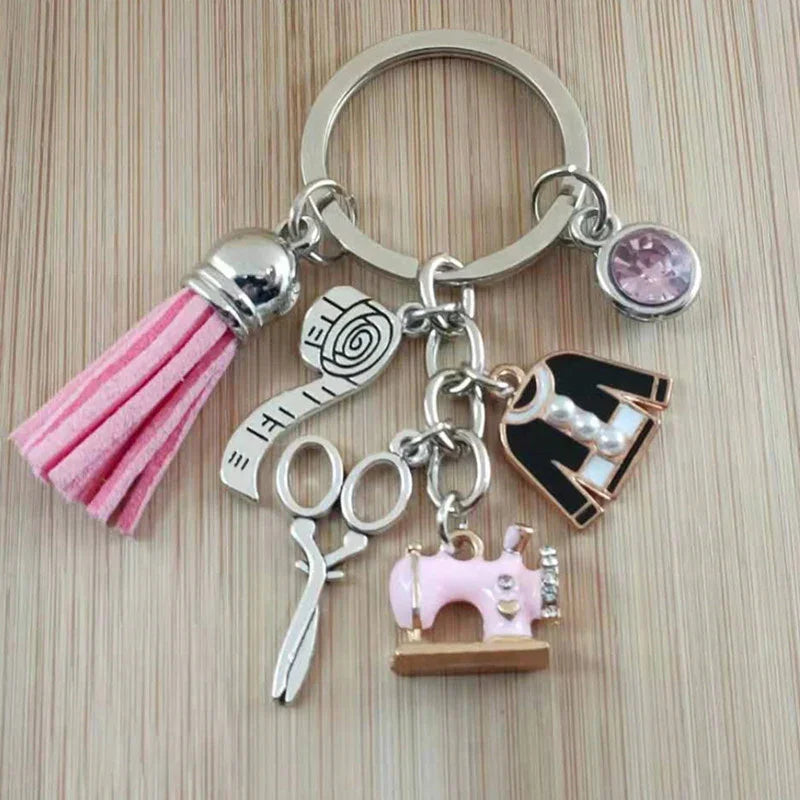 Fashion sewing themed keychain with pink tassel, measuring tape, scissors, pink sewing machine, dress, and pink gem