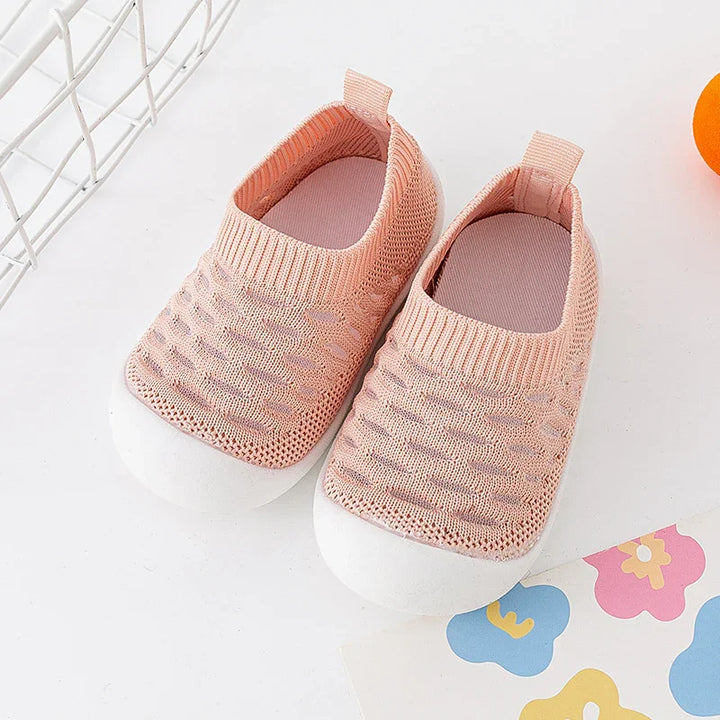 Pink knitted baby shoes with white soles on a white background with colorful flower print