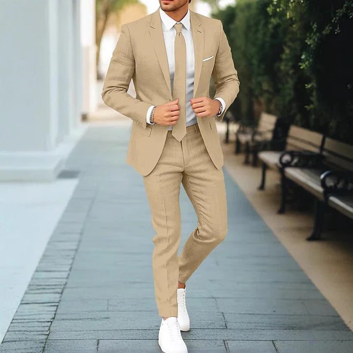 Man wearing beige suit, white shirt, and beige tie walking on outdoor pathway with benches