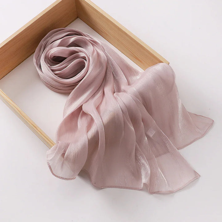 Light pink sheer chiffon scarf with a soft shimmer placed in a wooden tray on white background
