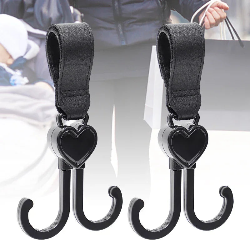 Pair of black heart-shaped stroller hooks with leather straps for hanging bags and accessories