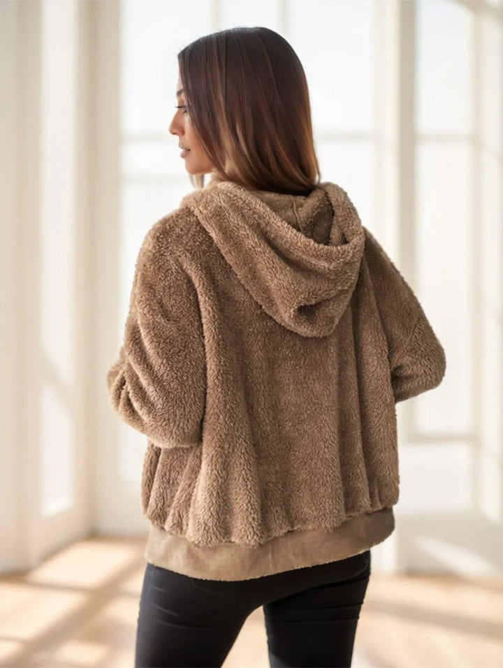 Woman wearing a cozy brown sherpa fleece hooded jacket indoors with natural light