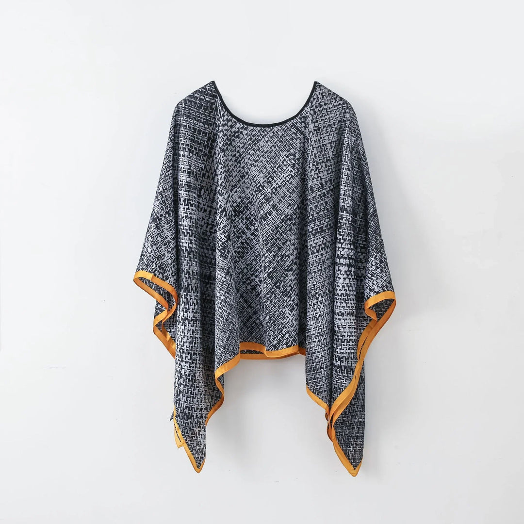 Black and white patterned poncho with orange trim hanging on white wall