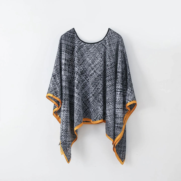 Black and white patterned poncho with orange trim hanging on white wall