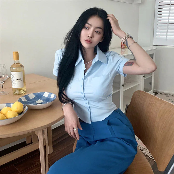 Young woman in light blue blouse and blue pants sitting at wooden table with lemons and wine bottle