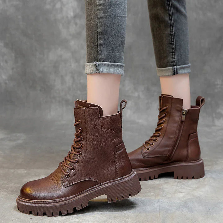 Brown leather lace-up combat boots with side zipper worn with rolled grey skinny jeans on concrete floor