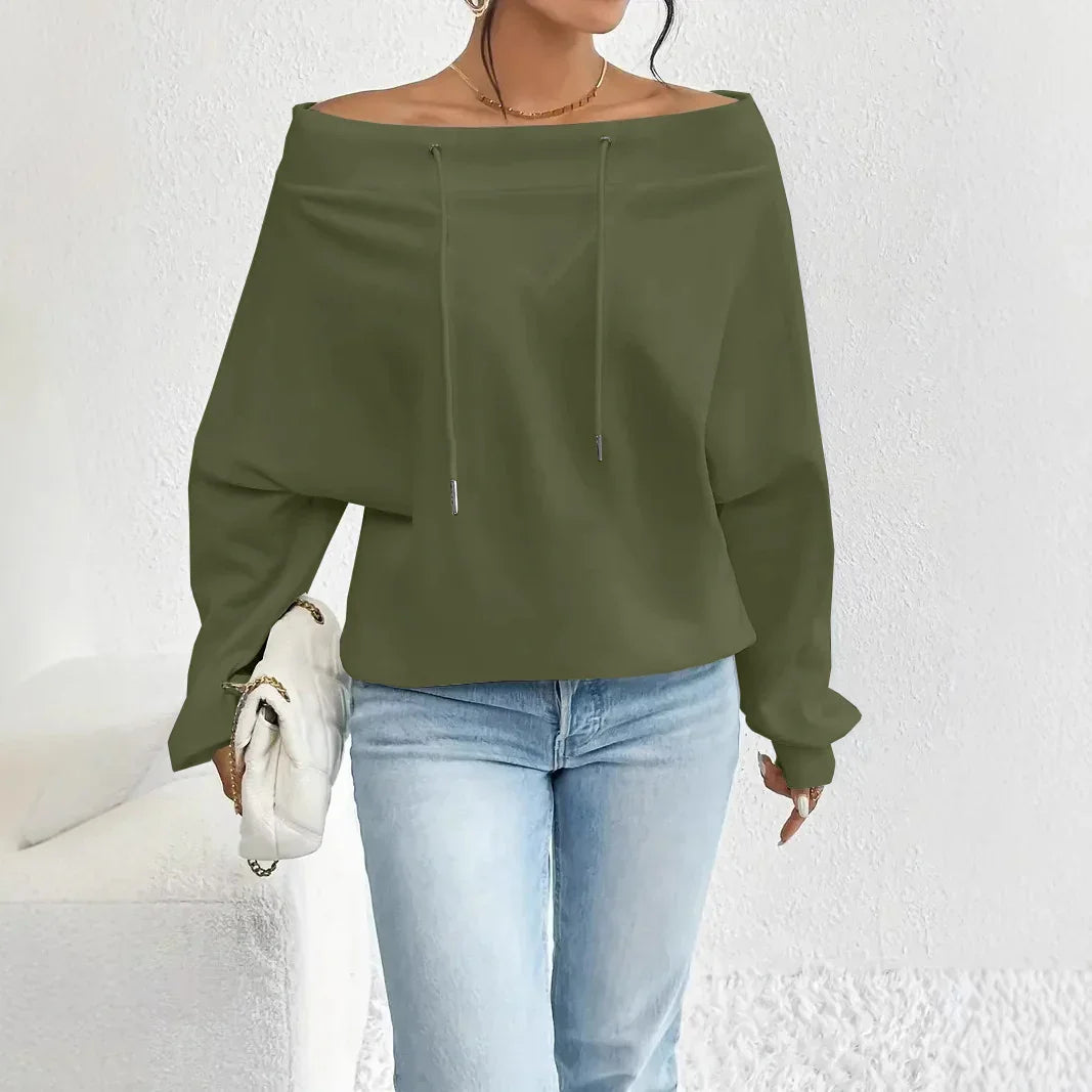 Woman wearing olive green off-shoulder sweatshirt and light blue jeans holding white clutch bag