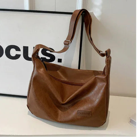 Brown leather shoulder bag with adjustable strap and front zipper pocket on white surface