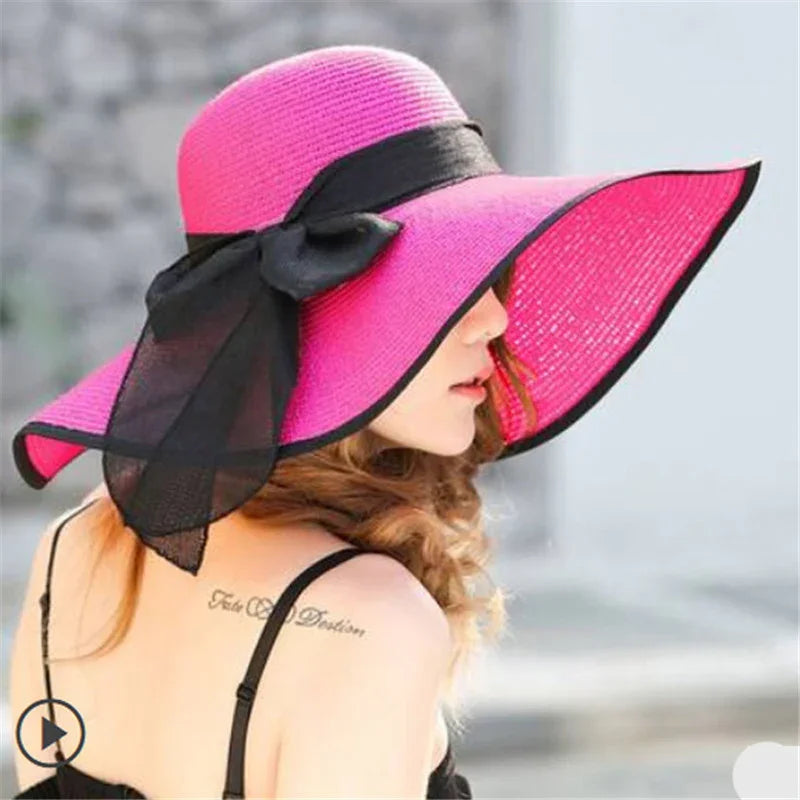 Woman wearing pink wide-brimmed sun hat with black ribbon bow, showing shoulder tattoo and black strap dress
