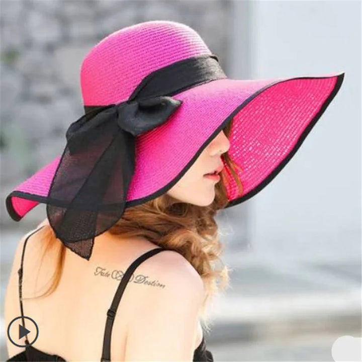 Woman wearing pink wide-brimmed sun hat with black ribbon bow, showing shoulder tattoo and black strap dress