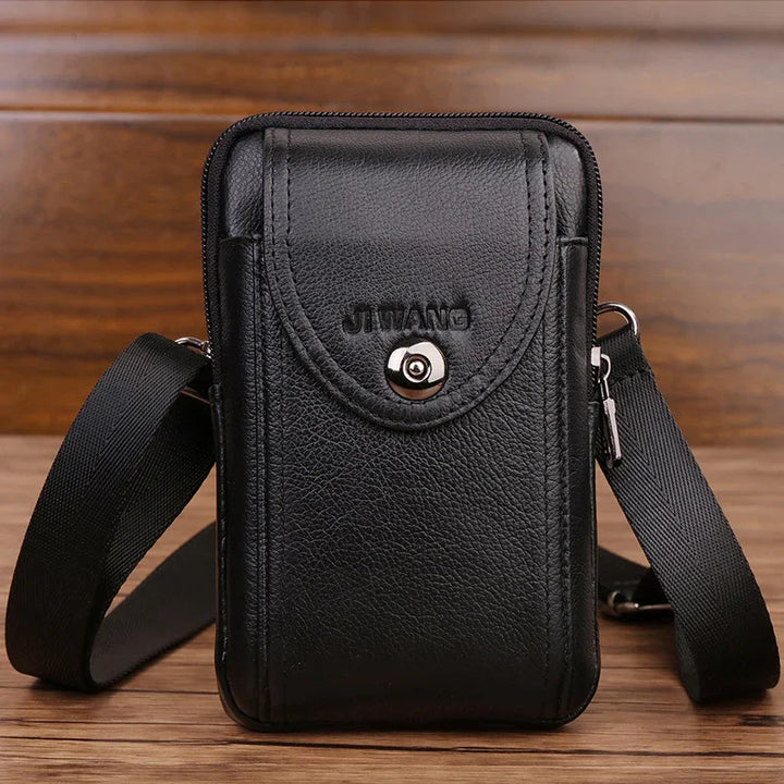 Black leather crossbody bag with front button pocket and adjustable strap on wooden surface
