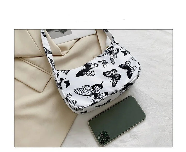 White shoulder bag with black butterfly print on beige fabric background next to a green smartphone