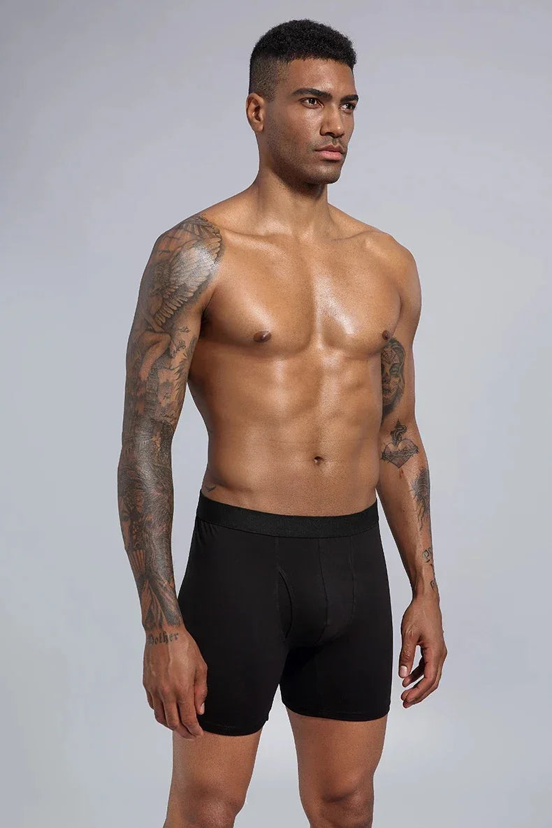 Fit tattooed man wearing black boxer briefs against plain gray background