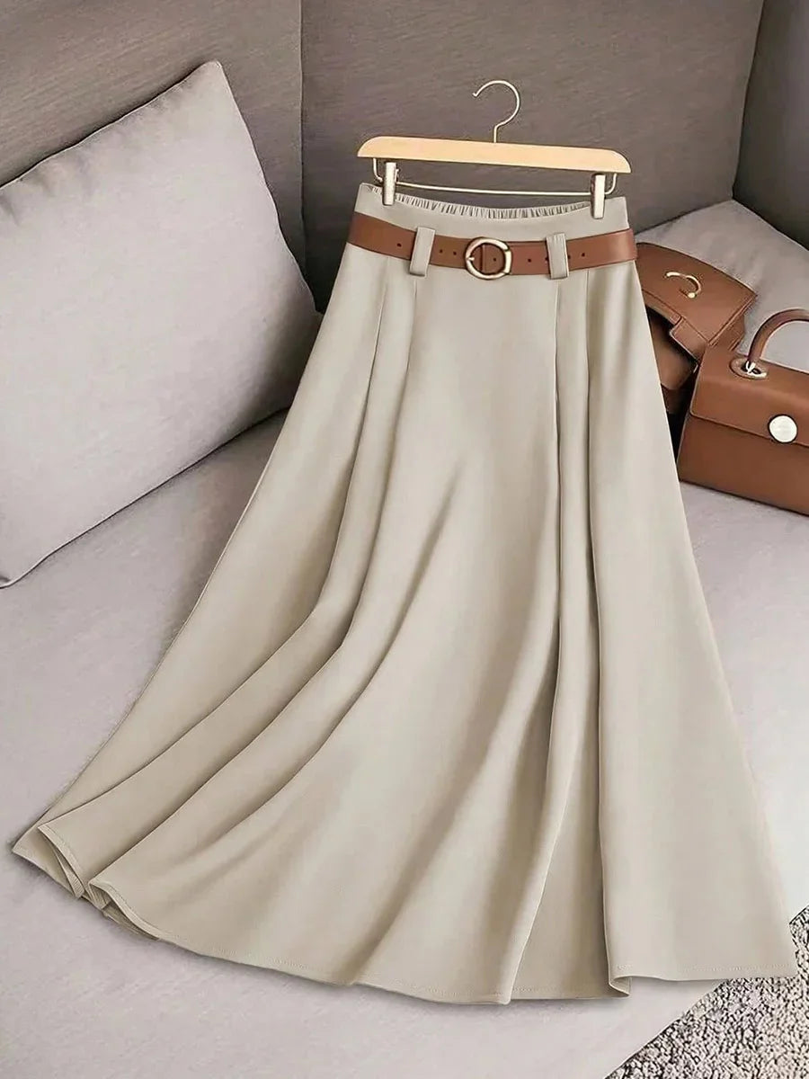Beige A-line skirt with brown belt on wooden hanger, displayed on light gray sofa with brown handbags