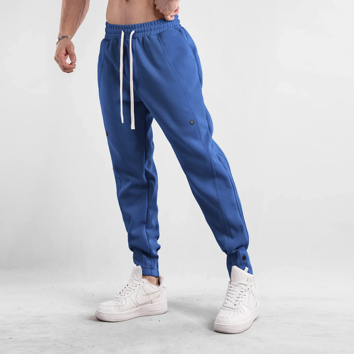 Male model wearing blue jogger pants with white drawstrings and white sneakers in studio