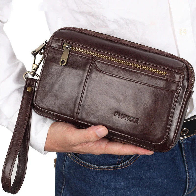 Hand holding dark brown leather wristlet clutch bag with zipper and embossed Piuncle logo