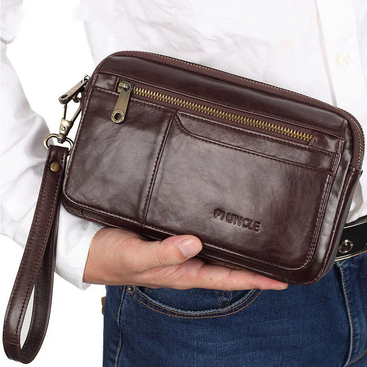 Hand holding dark brown leather wristlet clutch bag with zipper and embossed Piuncle logo