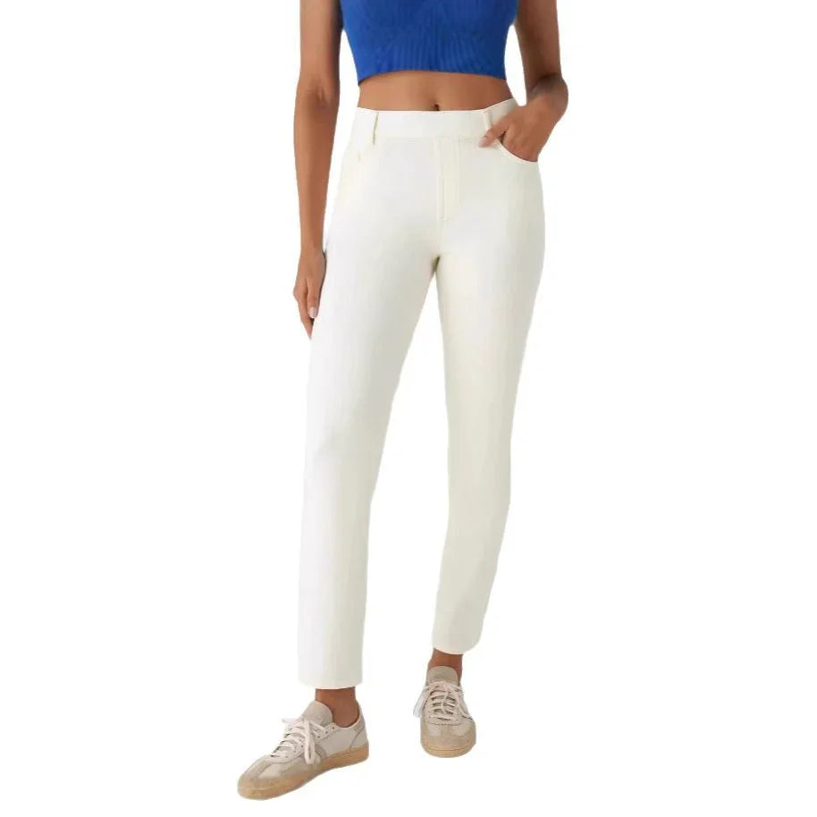 Woman wearing slim fit white pants, blue cropped top, and beige sneakers on white background