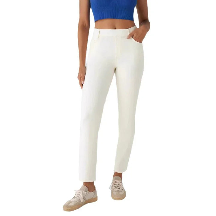 Woman wearing slim fit white pants, blue cropped top, and beige sneakers on white background