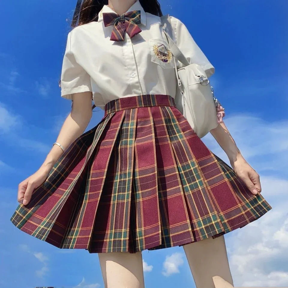Woman wearing a maroon and green plaid pleated skirt with white shirt and bow tie under blue sky