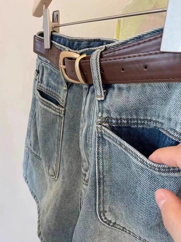 Blue denim jeans with front pockets and brown leather belt hanging on wooden hanger