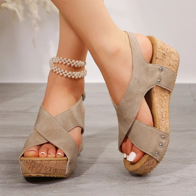 Women wearing suede wedge sandals with cork soles and pearl ankle bracelets on gray floor