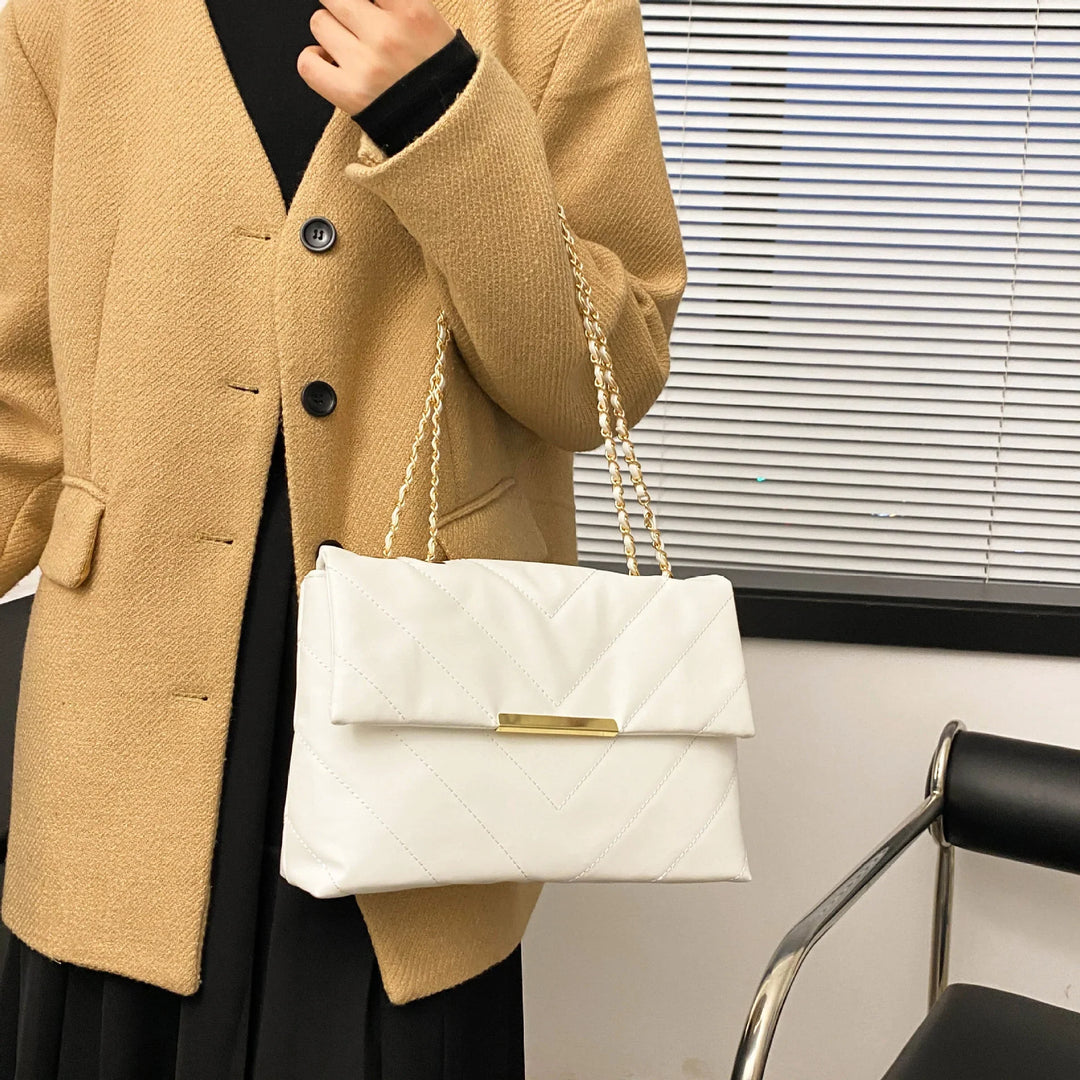 Woman wearing camel coat holding quilted white shoulder bag with gold chain straps