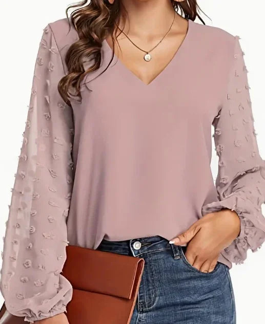 Woman wearing pink V-neck blouse with textured puff sleeves, blue jeans, and holding brown clutch