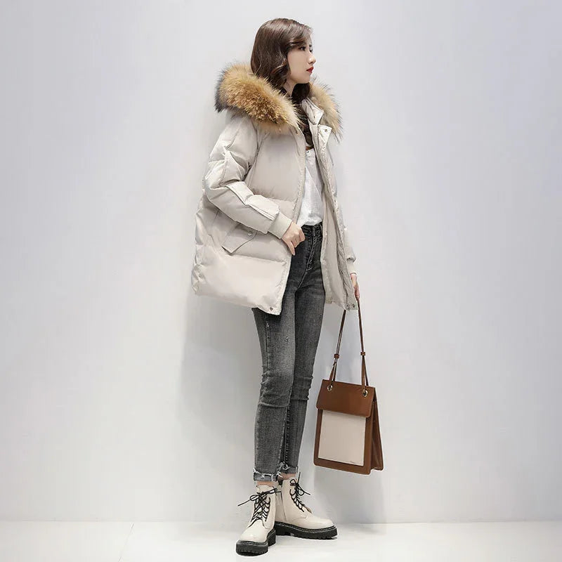 Woman wearing beige puffer jacket with fur hood, gray jeans, white boots, and carrying a brown handbag