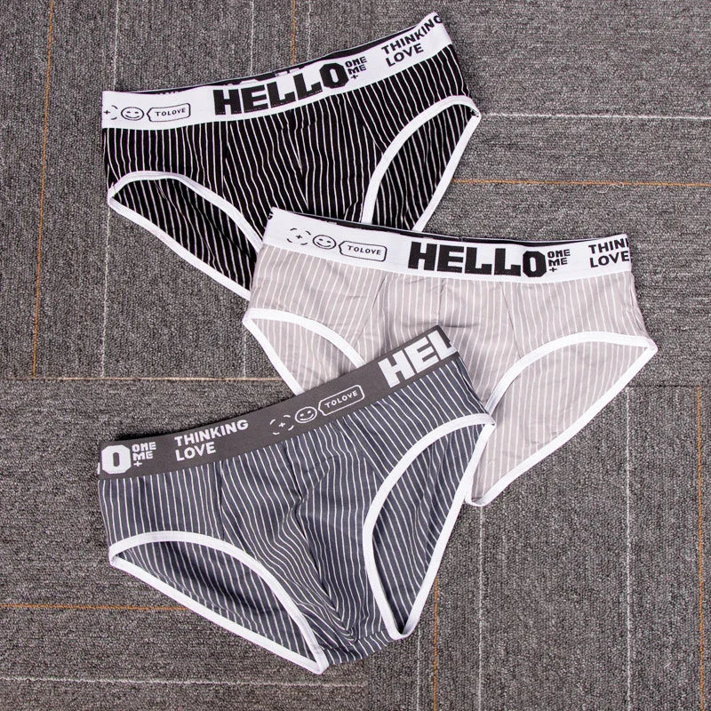 Set of three striped men's briefs in black, beige, and gray with white trim on gray carpet