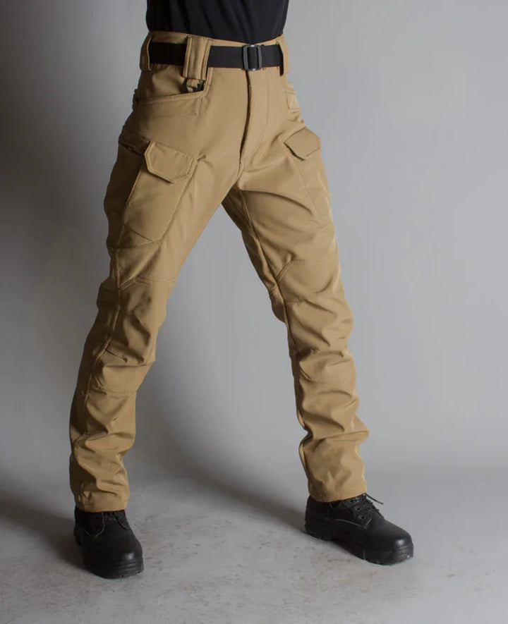 Person wearing tan tactical cargo pants with black belt and black boots against gray background