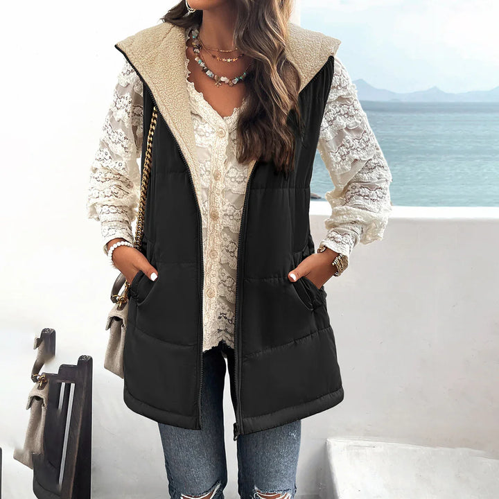 Woman wearing black sherpa-lined puffer vest over white lace blouse with ripped jeans by sea