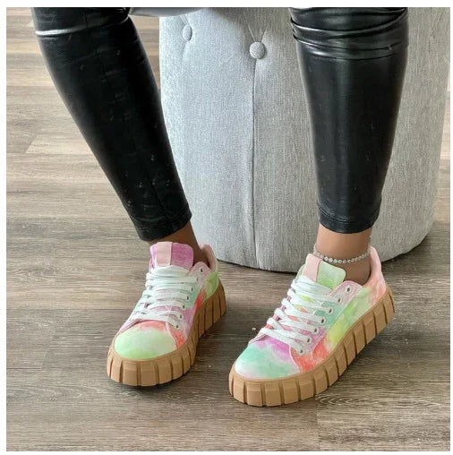 Tie-dye pastel platform sneakers with thick brown soles worn with black leather pants on wooden floor