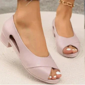 Close-up of feet wearing stylish light pink open-toe block heel shoes with gold anklet on beige floor
