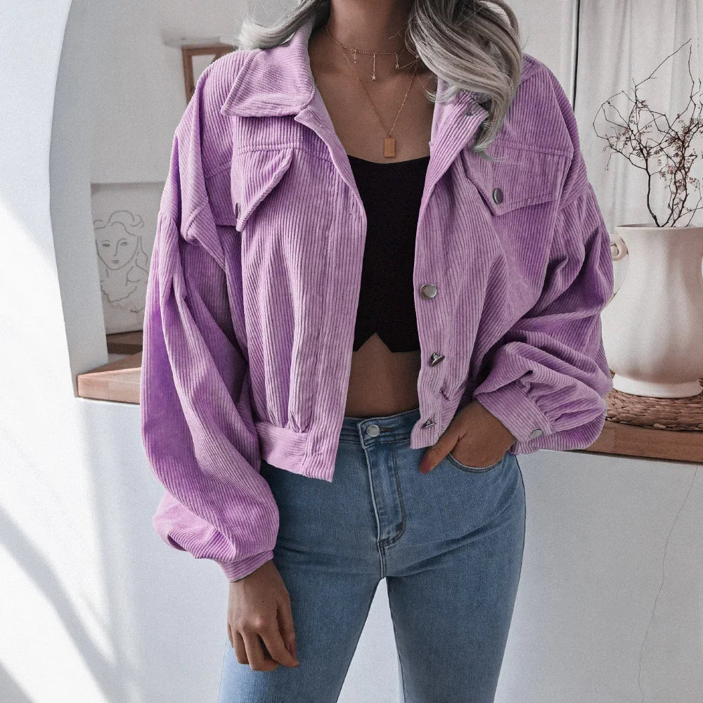 Woman wearing lavender corduroy cropped jacket with rolled sleeves, black crop top, and blue jeans indoors