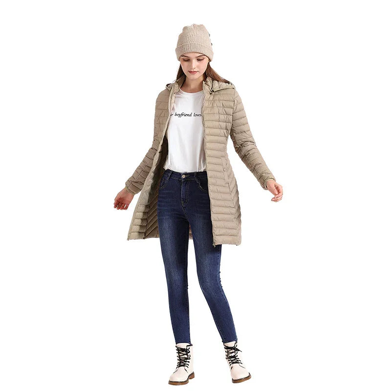 Woman wearing beige long puffer jacket, blue skinny jeans, white boots, and beige knit beanie on white background