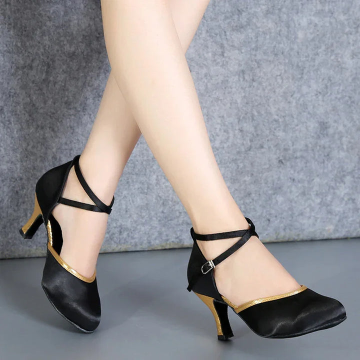 Black and gold satin high heel dance shoes with ankle straps on crossed legs