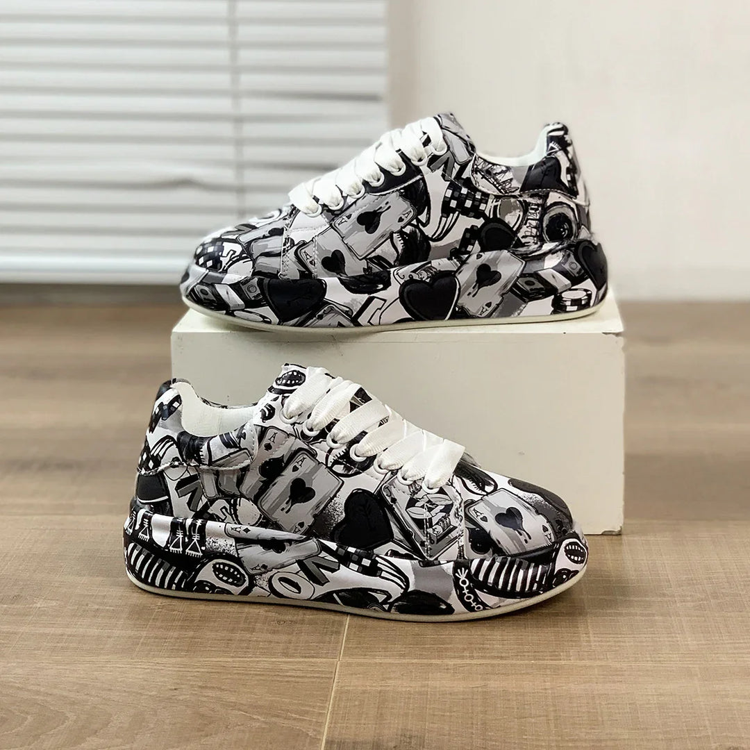 Pair of black and white sneakers with playing card and heart patterns on wooden floor and white box