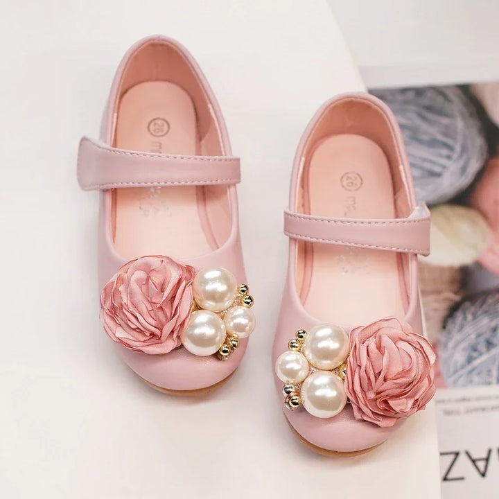 Pink girls' Mary Jane shoes with floral and pearl embellishments on a white surface