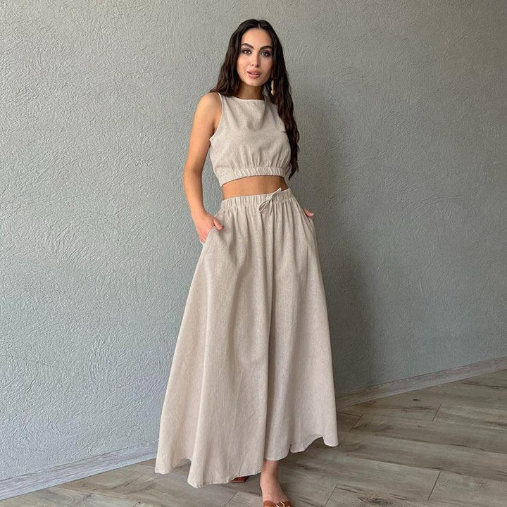 Woman wearing beige sleeveless crop top and matching wide-leg pants, standing indoors against gray wall