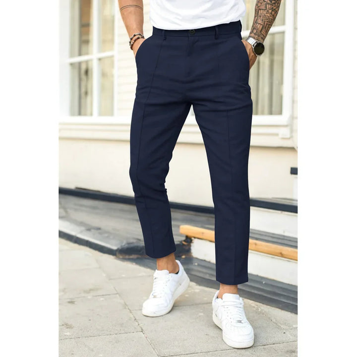 Man wearing slim fit navy blue trousers with white sneakers standing outdoors