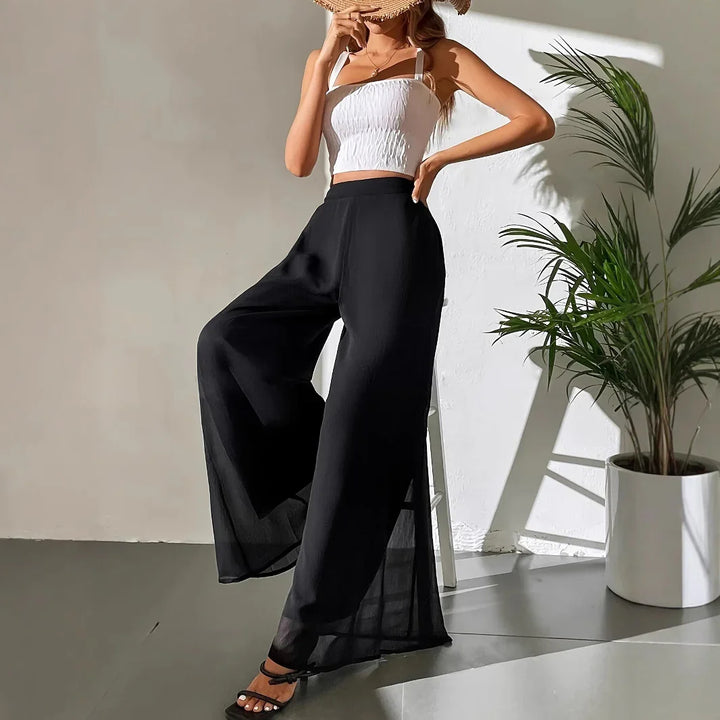 Woman wearing black wide-leg pants, white crop top, and straw hat in minimalist indoor setting