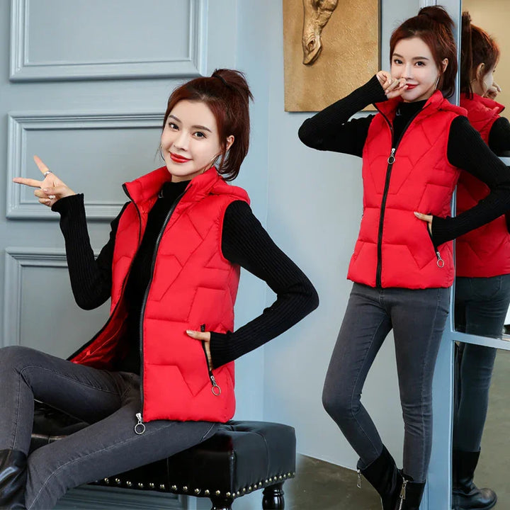 Woman wearing a bright red quilted vest over black top and gray jeans, posing indoors with a mirror reflection