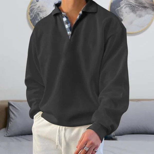 Man wearing black long sleeve polo shirt over checkered undershirt with beige pants in modern living room