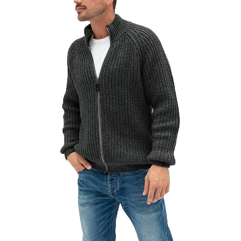 Man wearing dark gray knitted zip-up sweater and blue jeans against white background