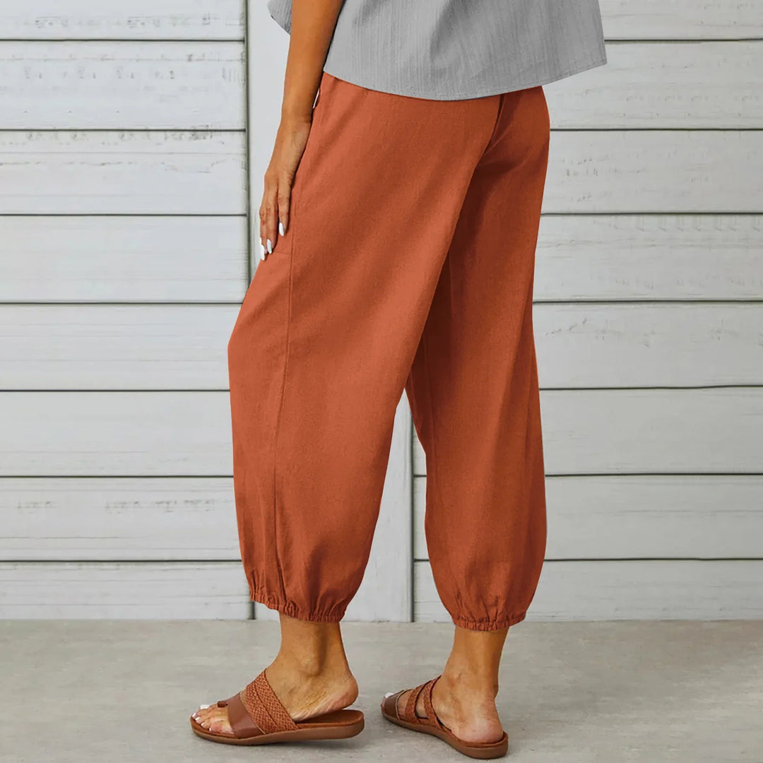Woman wearing rust-colored loose cropped pants with elastic cuffs and brown slide sandals