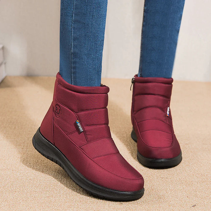 Red padded winter boots with black soles worn with blue jeans on beige carpet