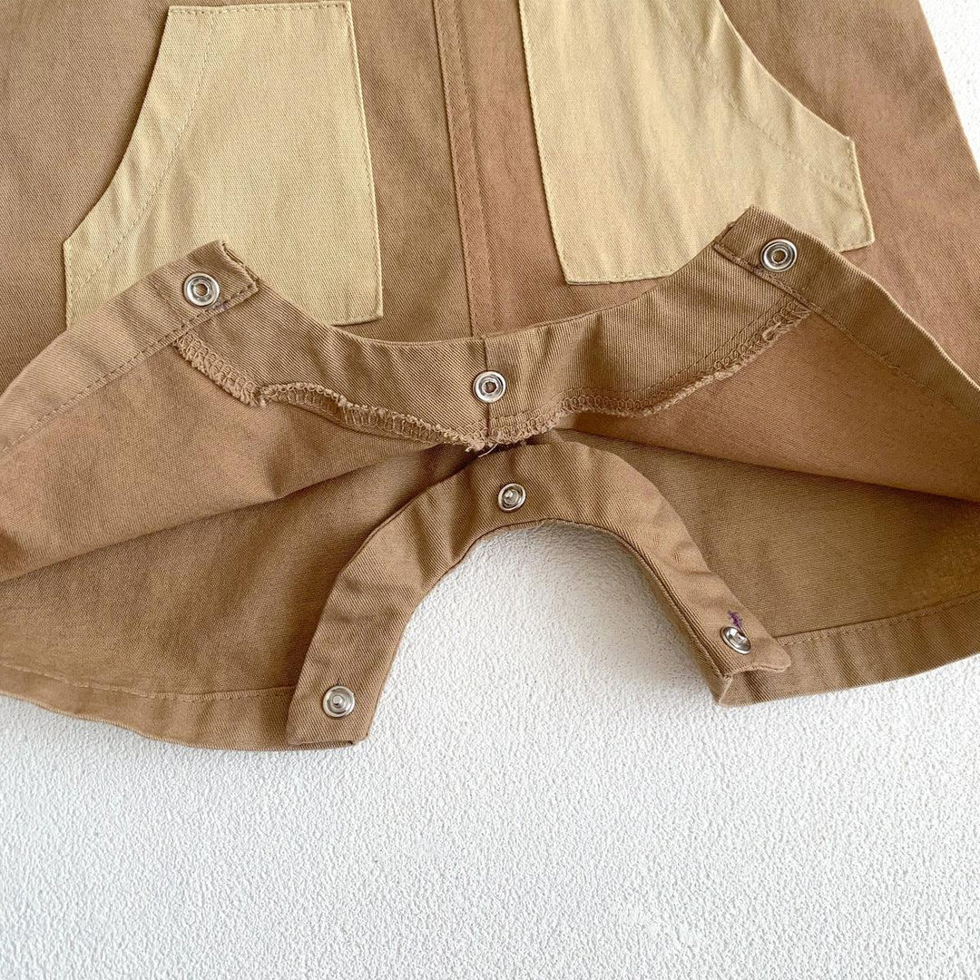 Close-up of brown and beige fabric with metal snap buttons and stitched pockets on textured white surface