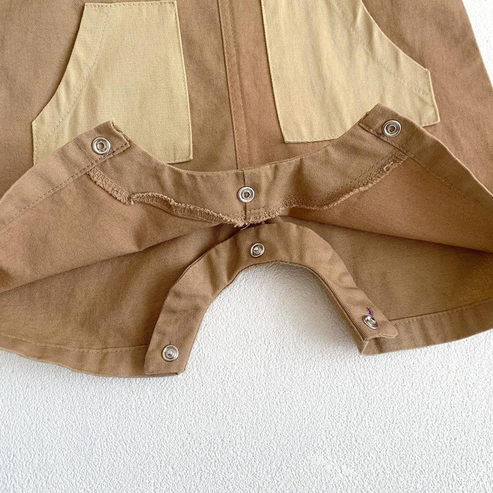 Close-up of brown and beige fabric with metal snap buttons and stitched pockets on textured white surface