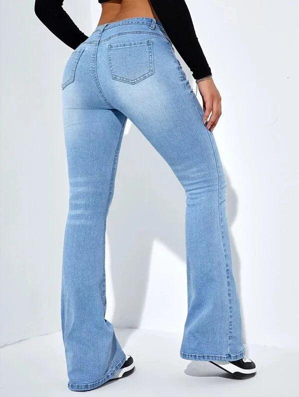 Woman wearing light blue high-waisted flare jeans and black crop top, posing against white background